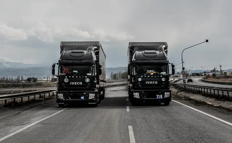 two black iveco trucks driving on a dual carriageway