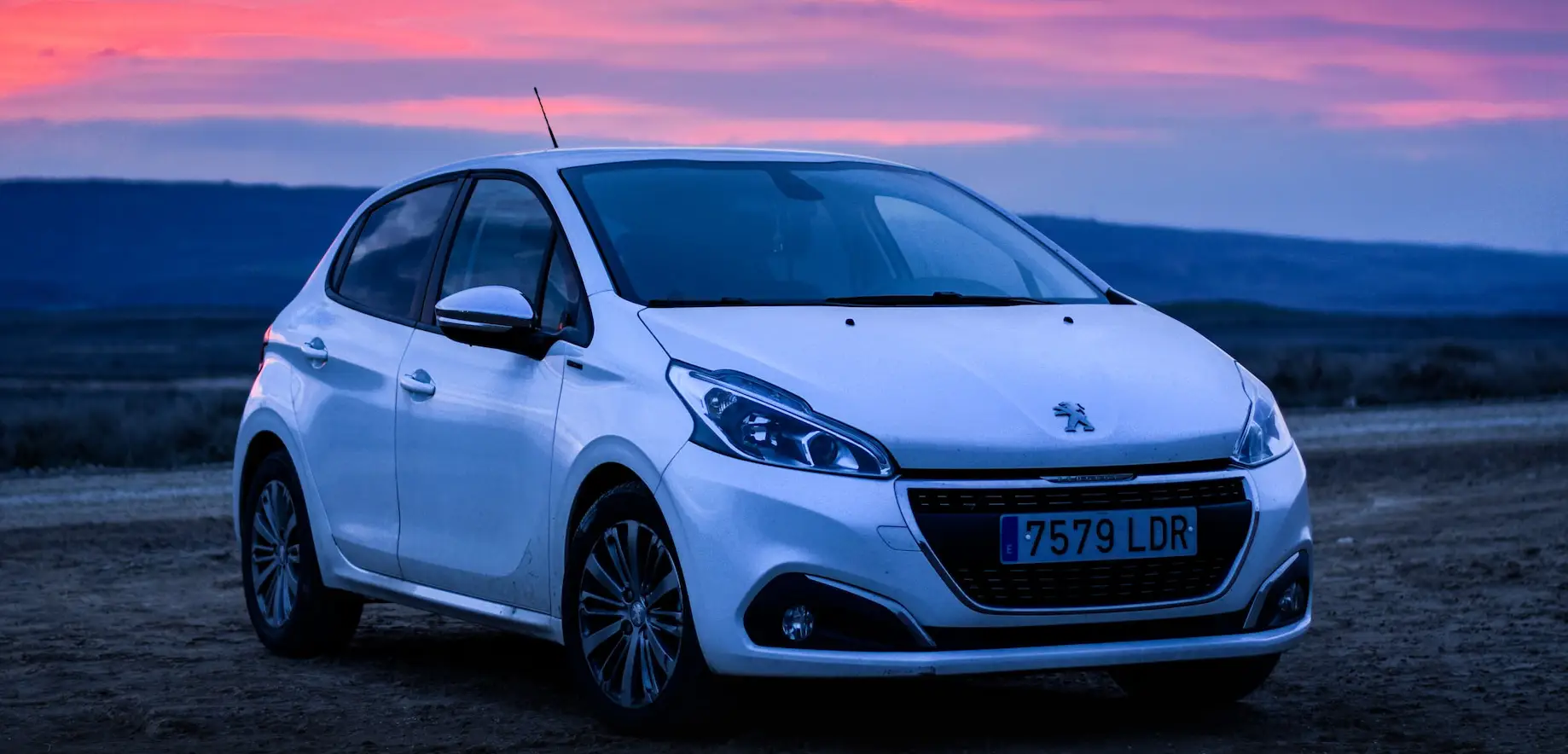 white peugeot car parked in front of a pink sunset