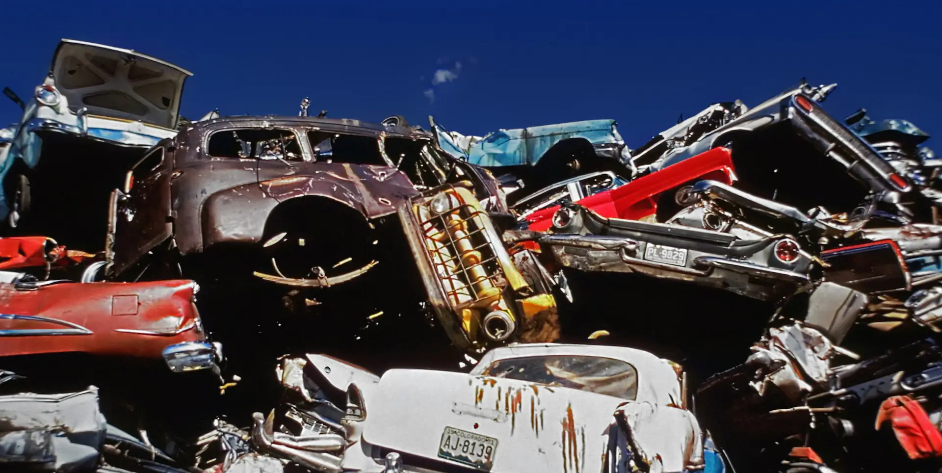 lots of scrapped cars piled up in front of a blue sky